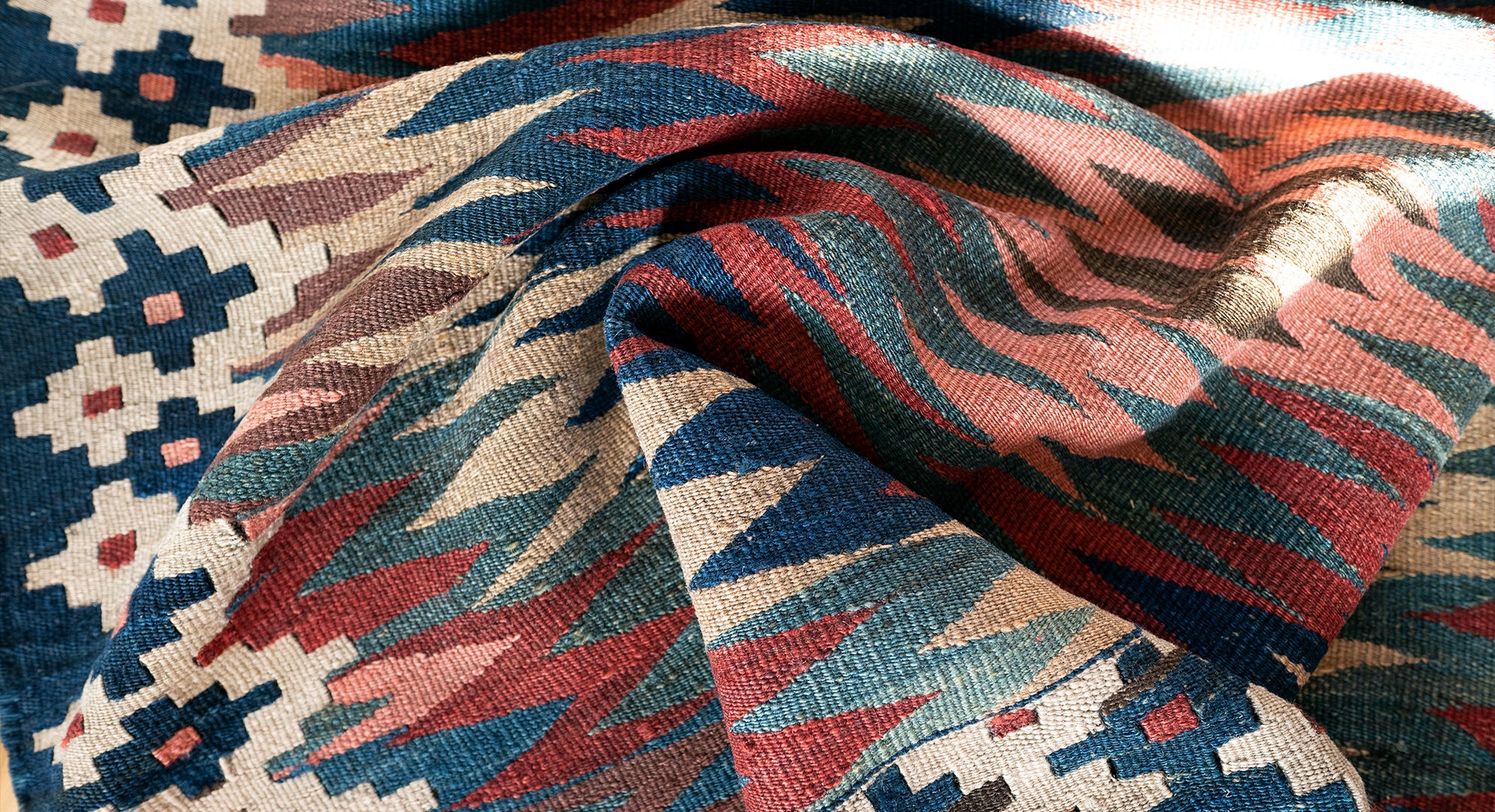 Folded handmade Persian antique kilim rug with geometric motifs in warm natural light, used as the hero banner for Oba Gallery.